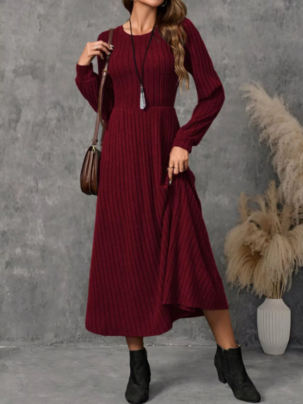 Burgundy ribbed knit long-sleeve A-line midi dress on a model holding the hem to one side.