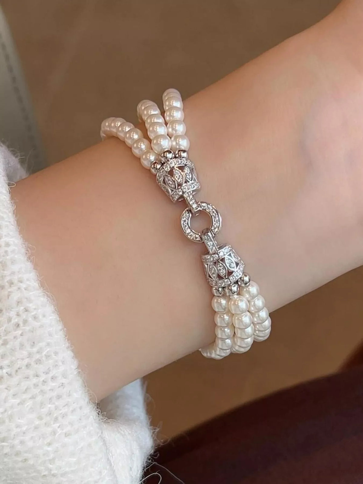 Close-up of a three-strand synthetic pearl bracelet with a decorative silver-colored fastening, worn on a wrist.