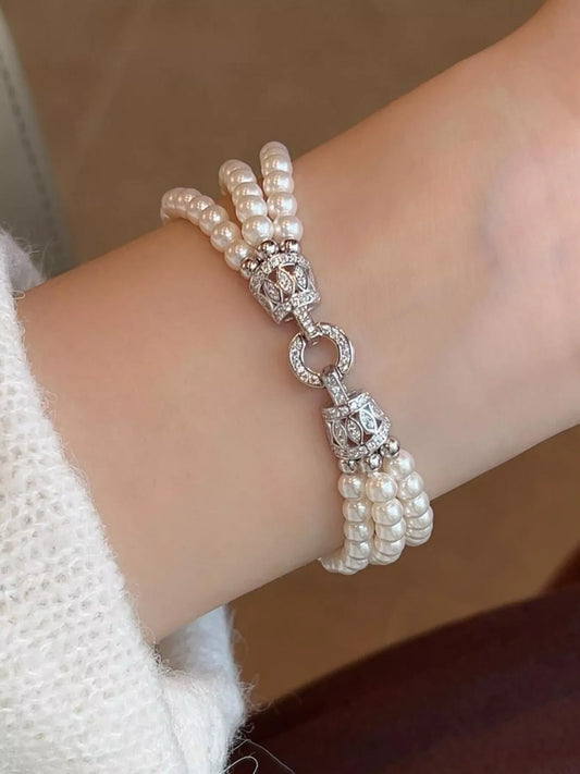 Close-up of a three-strand synthetic pearl bracelet with a decorative silver-colored fastening, worn on a wrist.