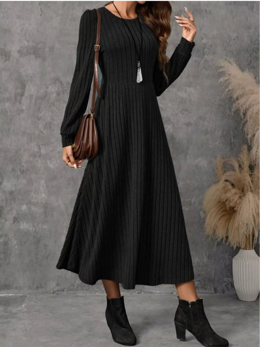 Black ribbed knit A-line midi dress with long sleeves, shown on a model carrying a brown shoulder bag.