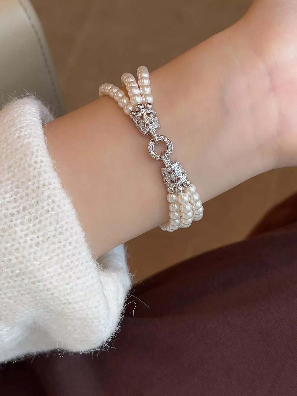 Three-strand synthetic pearl bracelet worn on a wrist, with its decorative silver-colored fastening facing upward.