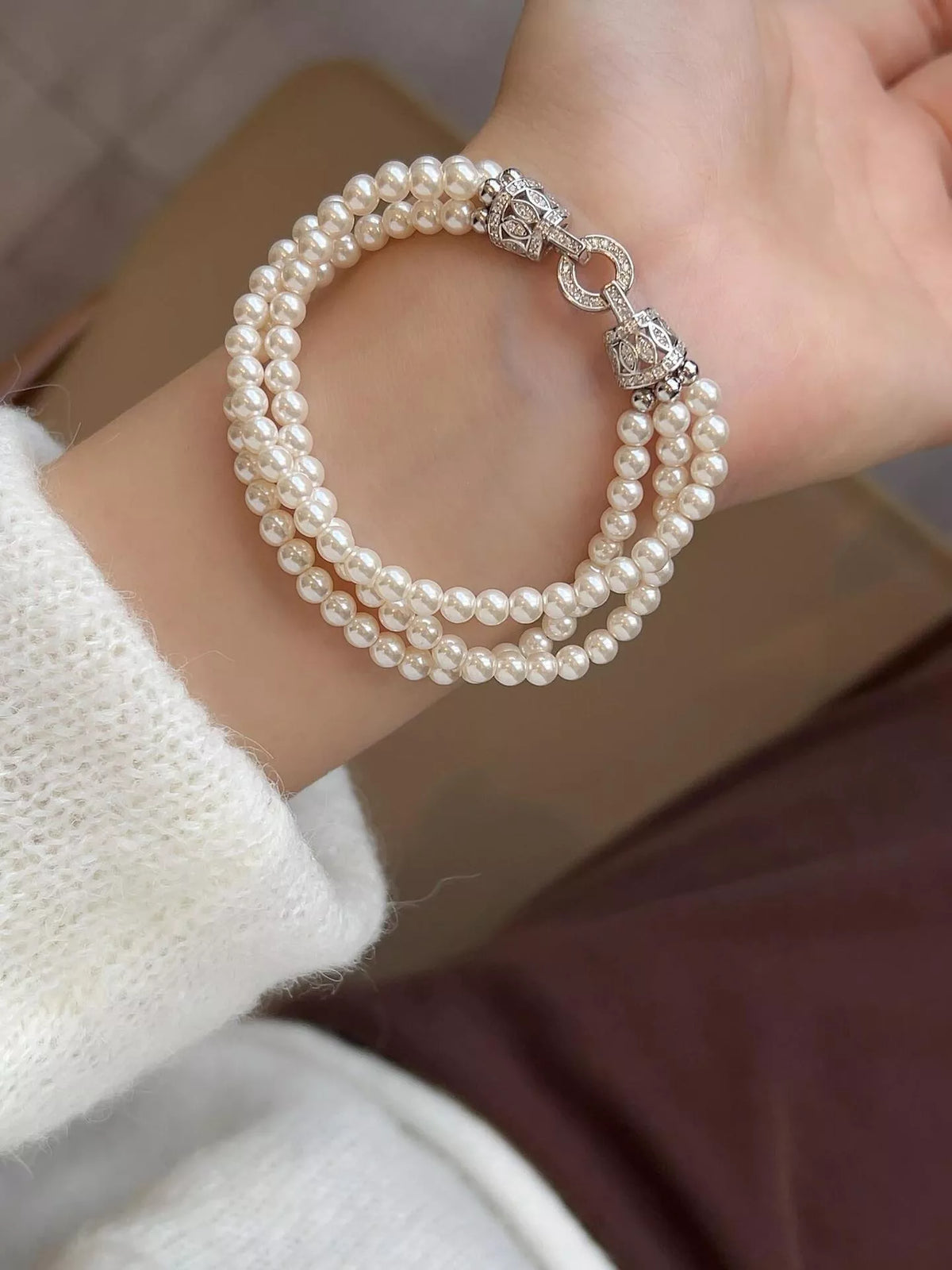 Three strands of synthetic pearls spread across a wrist, showing the bracelet’s decorative silver-colored fastening.