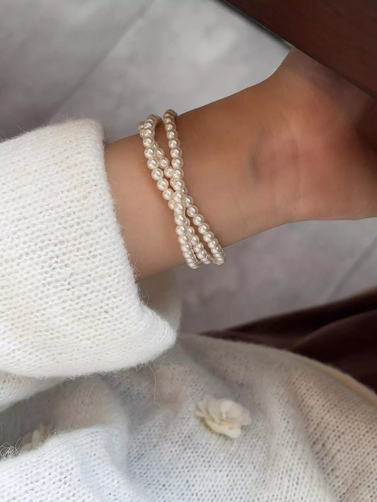 Side view of a three-strand synthetic pearl bracelet worn on a wrist beside a white knit sleeve.
